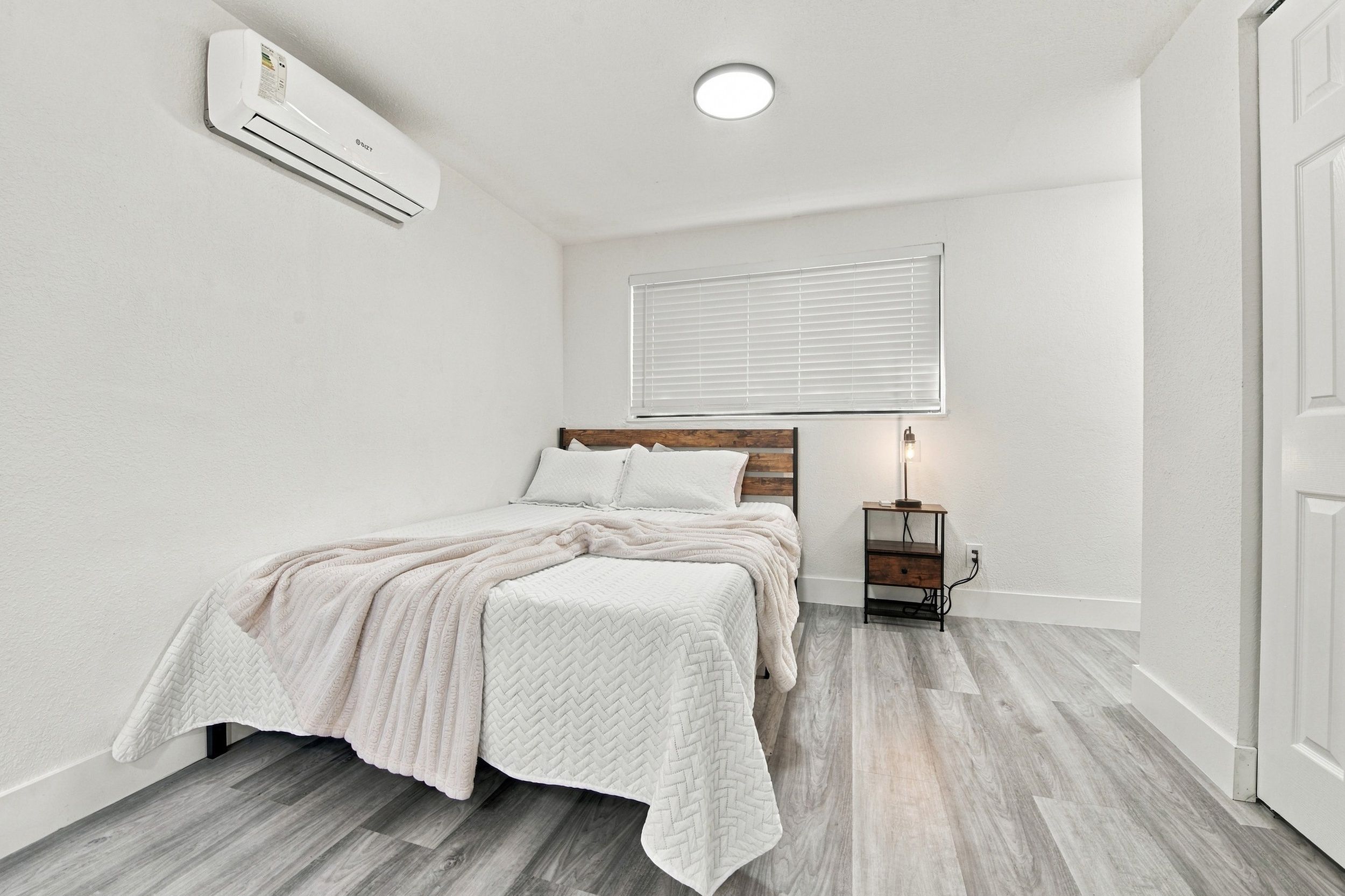 Une chambre à coucher comprenant un lit, une table de chevet, une lampe et un appareil de climatisation.