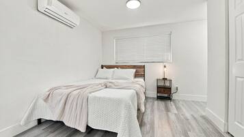 Un dormitorio con cama, mesita de noche, lámpara y aire acondicionado.