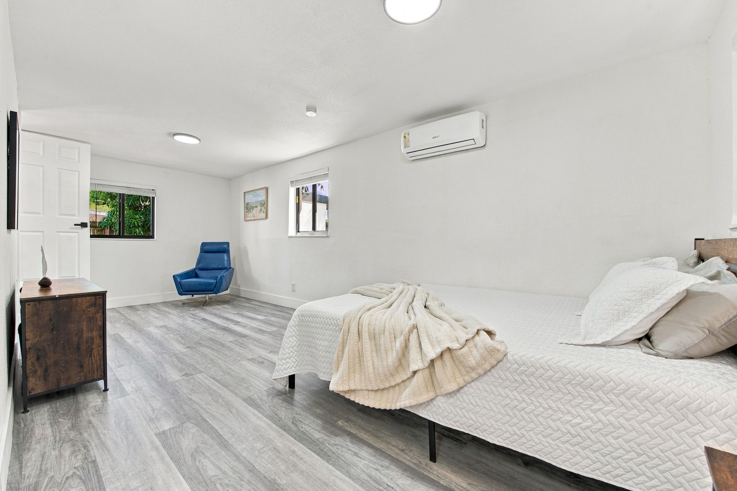A bedroom with a bed, a chair, a window, and an air conditioning unit.