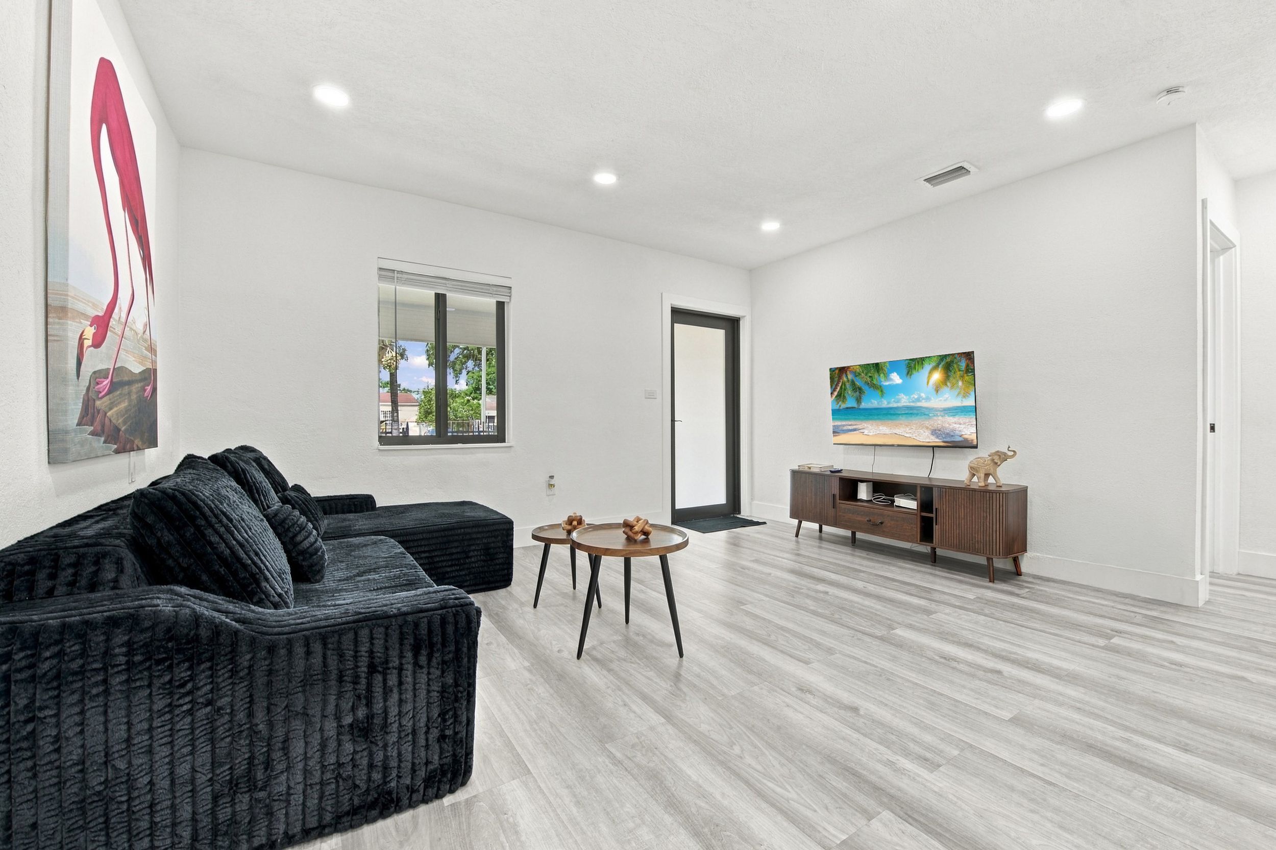 Una sala moderna con un sofá gris oscuro, una pequeña mesa redonda y un mueble de televisión de madera.
