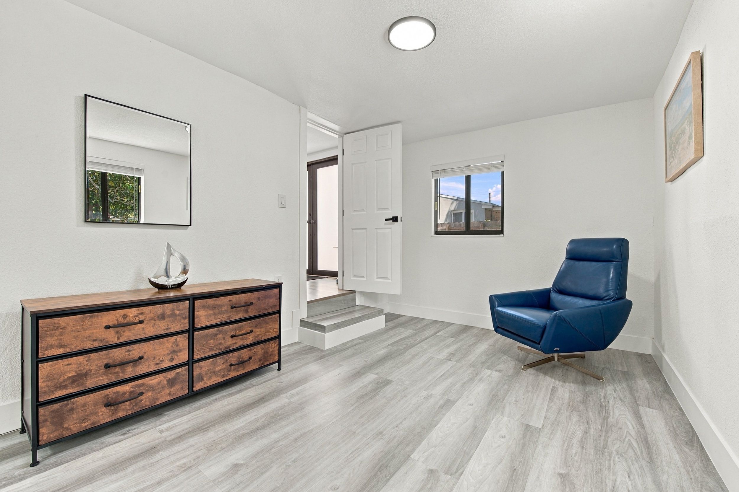 Un intérieur moderne avec une commode en bois, un fauteuil en cuir bleu et un couloir menant à une porte.