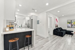 A modern kitchen with a central island, bar stools, and a dining area with a black sofa and a table. - Casa Miami (Miami)