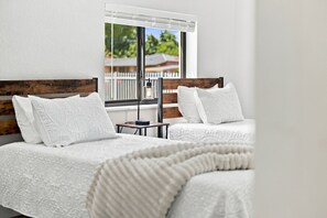 A hotel room with two beds, each with white linens and a wooden headboard. There is a window with a view of greenery outside. - Casa Miami (Miami)