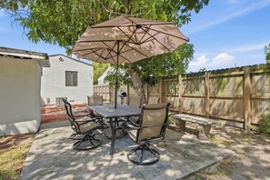 An outdoor patio with a table and chairs, a large umbrella, and a wooden fence in the background.