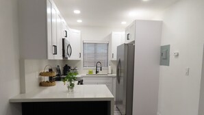 Cozinha moderna com armários brancos, geladeira de aço inoxidável e uma pequena ilha com banquetas.