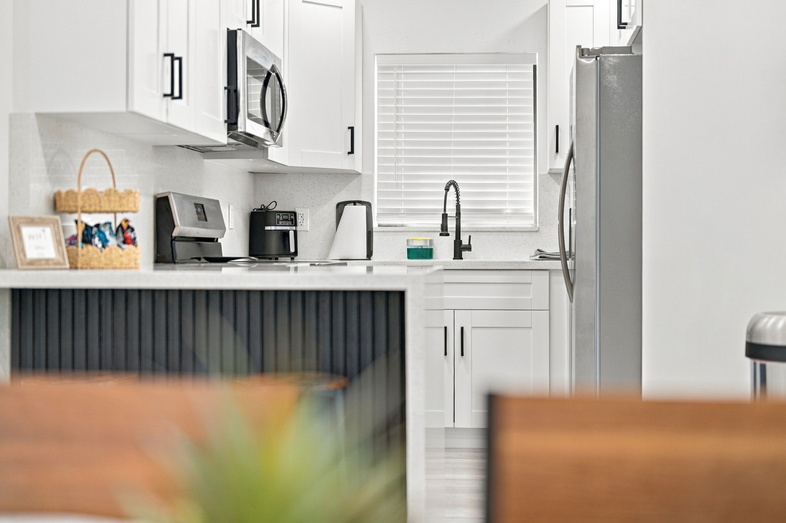 A modern kitchen with white cabinets, a microwave, a coffee maker, and a refrigerator.