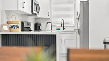 A modern kitchen with white cabinets, a microwave, a coffee maker, and a refrigerator.