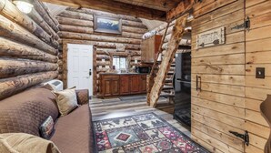 L’intérieur d’une cabane en rondins présente un espace de vie chaleureux, une cuisine avec des meubles en bois et un escalier menant à un autre niveau.