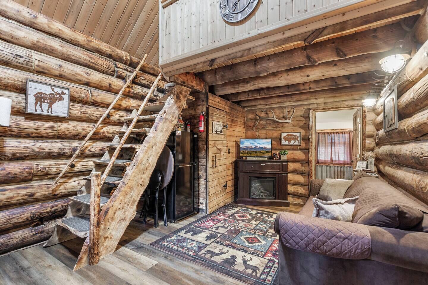 A log cabin interior with a wooden staircase, a fireplace, a television, and a cozy seating area.