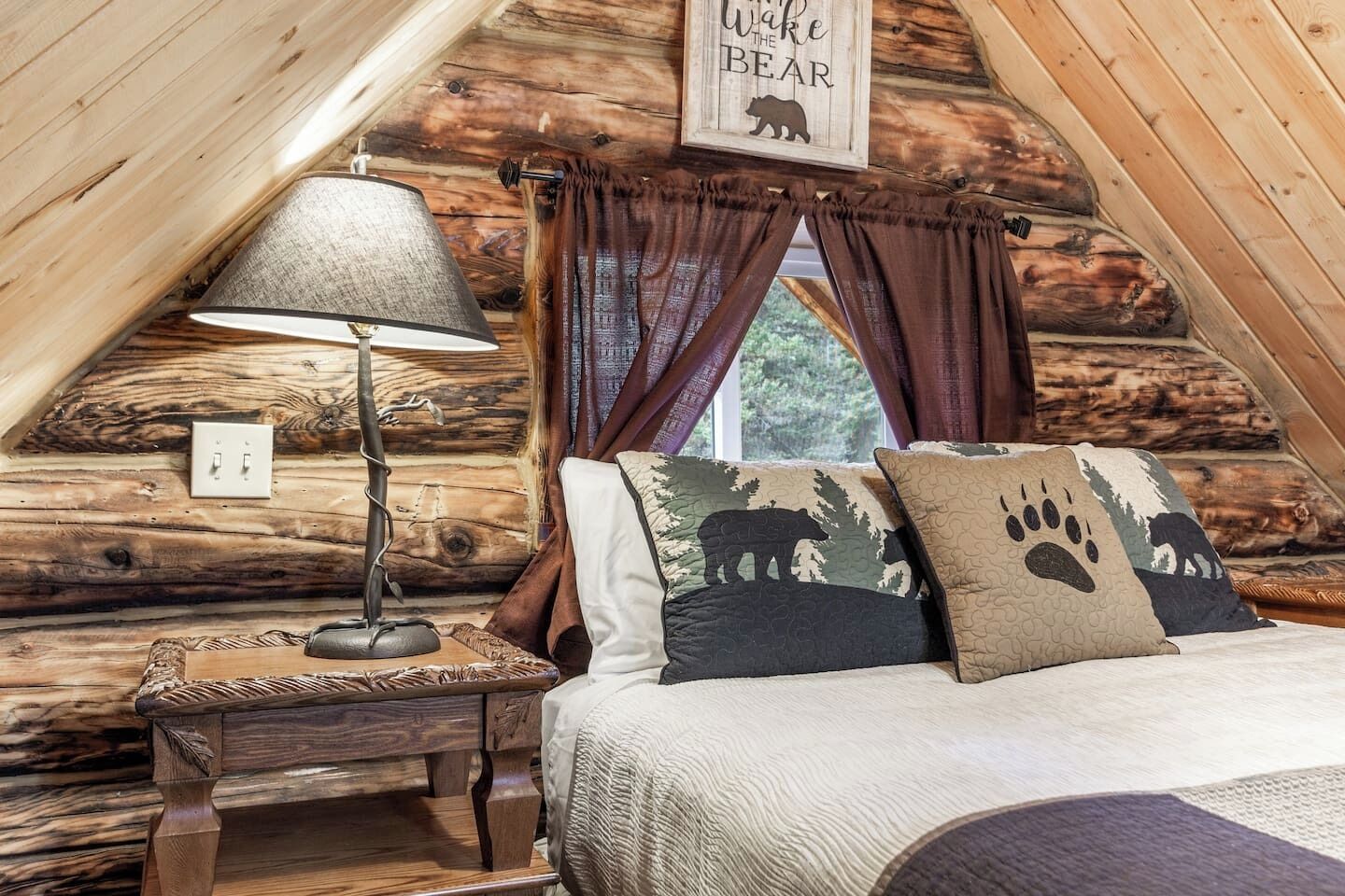 A cozy log cabin bedroom with a bed, a lamp, and a window with curtains.