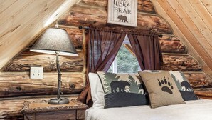 Une chambre confortable dans un chalet en rondins, avec un lit, une lampe et une fenêtre avec des rideaux.