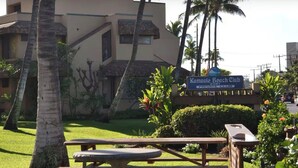 Un panneau indiquant l’entrée d’un club de plage privé, des palmiers et une zone herbeuse avec une table de pique-nique.