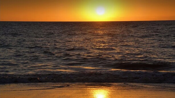 Un coucher de soleil sur l’océan, avec des vagues qui se rapprochent du rivage.