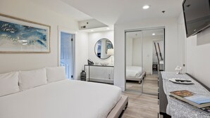 Moderni hotellihuone, jossa on suuri sänky, peilillä varustettu työpöytä ja televisio.