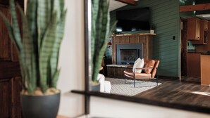 A modern living room with a fireplace, leather armchair, and a large potted plant. - Designer | Hot Tub | Gameroom | Firepit | Sleeps12 (Banner Elk)