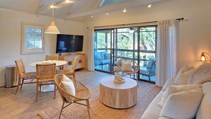 Amplia sala de estar con techo alto, ventiladores de techo, televisor grande y un espacio de descanso cómodo con sofá y sillones.