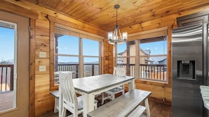 A wooden cabin interior with a dining table, chairs, a bench, a chandelier, and a refrigerator. - 3BR | Long Range Views | Hot Tub | Minutes to Pkwy (Sevierville)