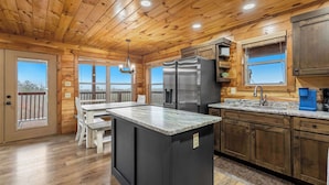 A wooden cabin kitchen with a central island, wooden cabinets, and a large window. - 3BR | Long Range Views | Hot Tub | Minutes to Pkwy (Sevierville)