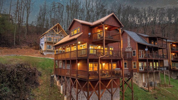 A multi-story log cabin with balconies and a stone foundation, surrounded by trees. - 3BR | Long Range Views | Hot Tub | Minutes to Pkwy (Sevierville)