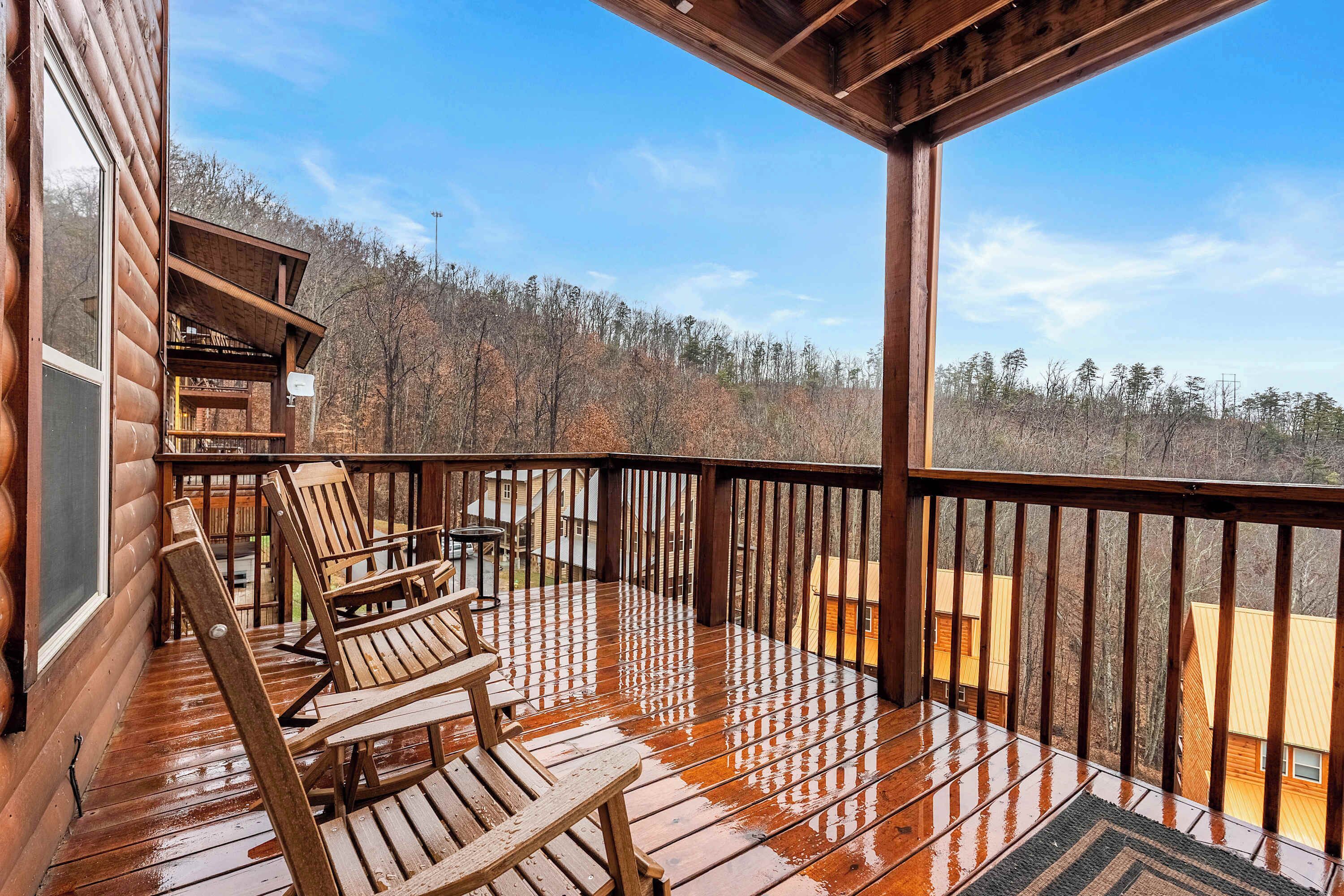 A wooden deck with chairs and a table, overlooking a forested area.