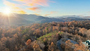 A mountainous landscape with autumn foliage, a winding road, and a house with a green roof. - Hot Tub, Game Loft, Open Living, Minutes to Downtown Gatlinburg Whisper Cabin by Avantstay (Gatlinburg)