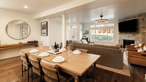 A modern dining area with a wooden table set for four, a round mirror, and a stone fireplace. - Year-round Altitude Adjustment, Private Hot Tub, Community Amenities, Walk to Restaurants and more! (Park City)