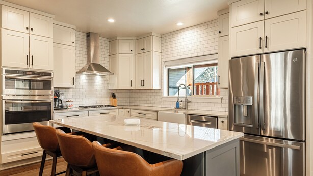 A modern kitchen with white cabinets, stainless steel appliances, a large island with bar stools, and a window with a view of the outside. - Year-round Altitude Adjustment, Private Hot Tub, Community Amenities, Walk to Restaurants and more! (Park City)