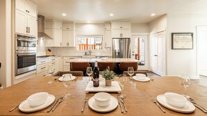 A modern kitchen with white cabinets, stainless steel appliances, and a wooden dining table set for four. - Year-round Altitude Adjustment, Private Hot Tub, Community Amenities, Walk to Restaurants and more! (Park City)