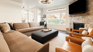 A living room with a sectional sofa, ottoman, leather armchairs, a flat-screen TV mounted on a stone wall, and a fireplace. - Year-round Altitude Adjustment, Private Hot Tub, Community Amenities, Walk to Restaurants and more! (Park City)