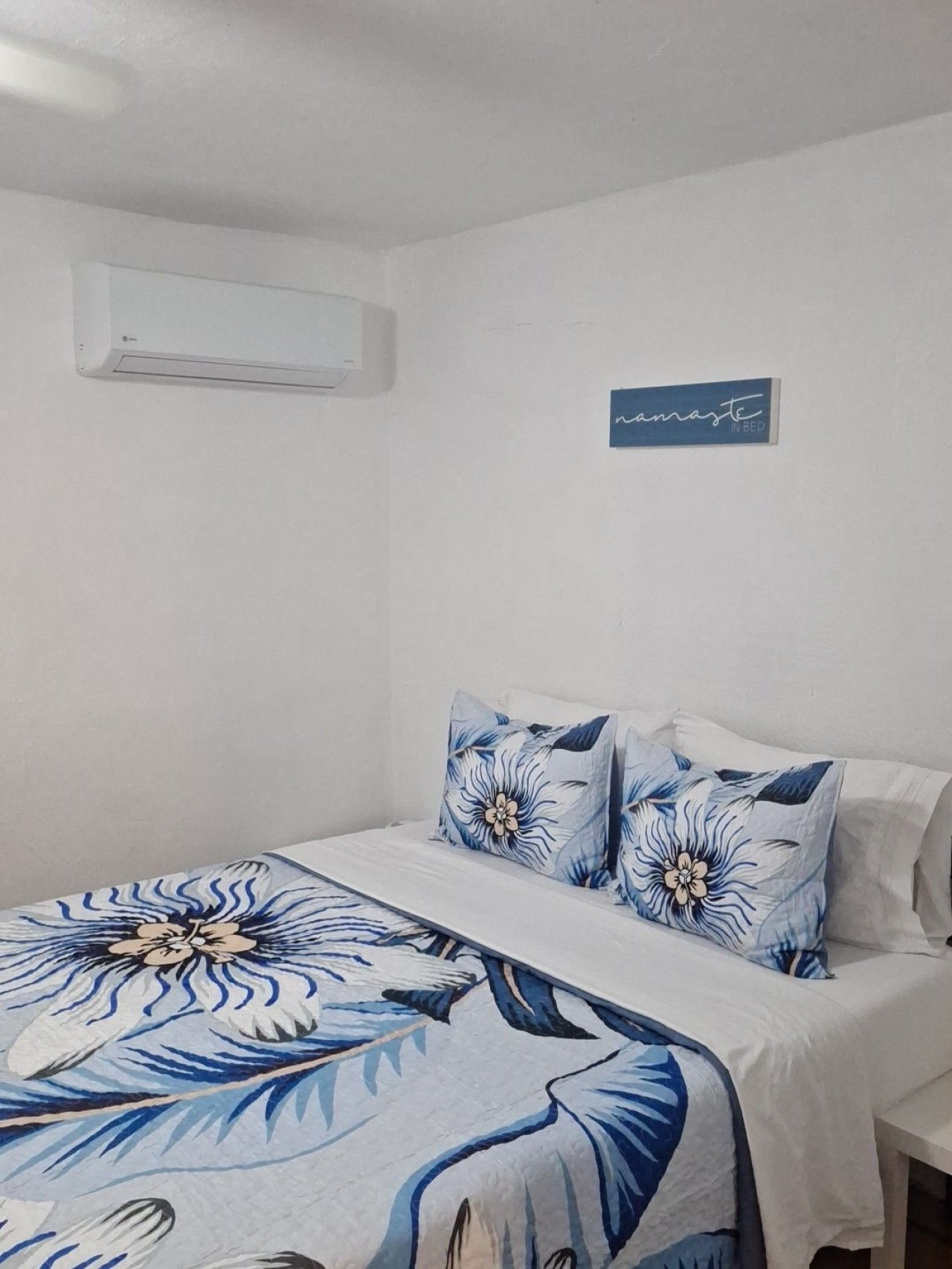 A bedroom with a bed, pillows, a wall-mounted air conditioner, and a sign on the wall.