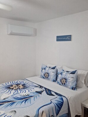 A bedroom with a bed, pillows, a wall-mounted air conditioner, and a sign on the wall. - La Iguana Morada: A/C, WiFi, BioBay, walk to Ferry (Vieques)