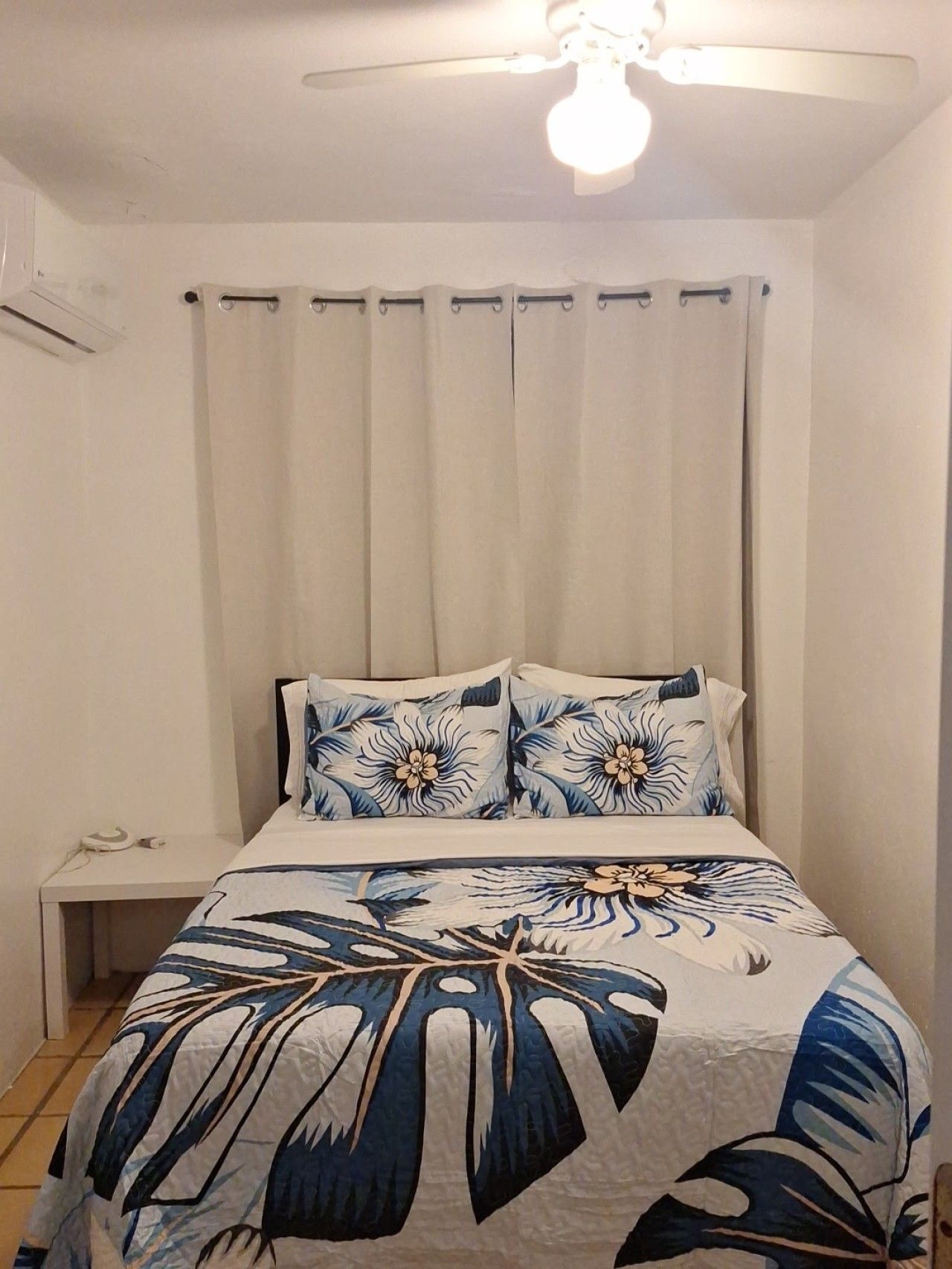 A bedroom with a bed, a nightstand, a ceiling fan, and a window with curtains.