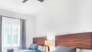 A hotel room with two beds, a ceiling fan, a nightstand with a lamp, and a window with curtains.