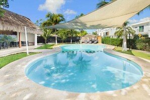 Ein Swimmingpool mit einer strohgedeckten Struktur, Palmen und einem weißen Gebäude im Hintergrund.