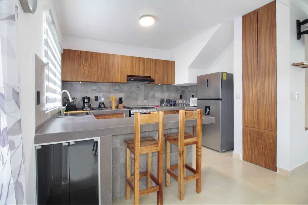 A modern kitchen with wooden cabinets, a stainless steel refrigerator, and a built-in island with bar stools.