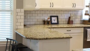 A kitchen with white cabinets, a granite countertop, and a small island with stools. - Reed's Ranch House In Star (Star)
