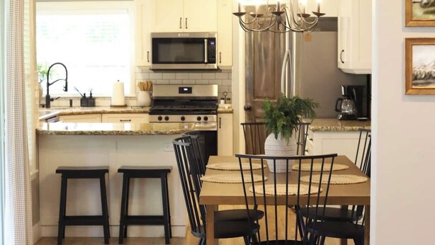 A modern kitchen with white cabinets, a microwave, and a chandelier. There is a dining area with a table and chairs, and a sofa in the foreground. - Reed's Ranch House In Star (Star)