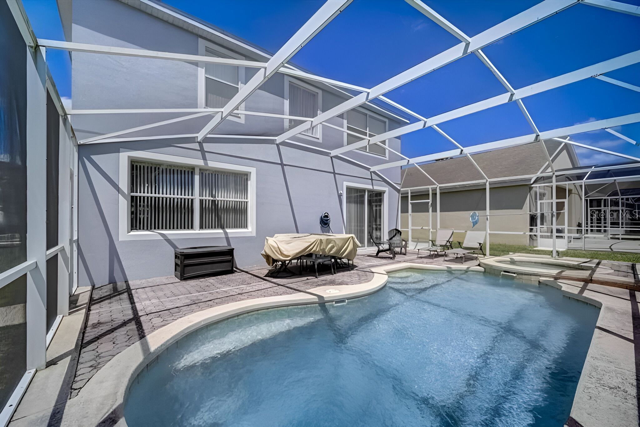 Ein Schwimmbad mit überdachter Terrasse, Grillmöglichkeit und überdachter Sitzgruppe mit Tisch und Stühlen.