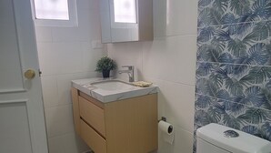 Casa de banho com sanita, lavatório e espelho. Existem duas janelas e uma planta num vaso sobre a bancada.