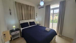 Quarto com cama, mesas de cabeceira, luminária e vista para o exterior.