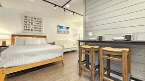 A hotel room with a bed, a sofa, two bar stools, a kitchen counter, and a wall with a heart-shaped artwork. - WG 300 — Cozy Queen Bed Studio 2 mins Walk to Waikiki Beach (Honolulu)