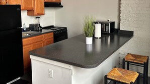 A kitchen with wooden cabinets, a black refrigerator, a stove, and a small island with stools. - Detroit Studio Loft Cozc Private Entry (Detroit)