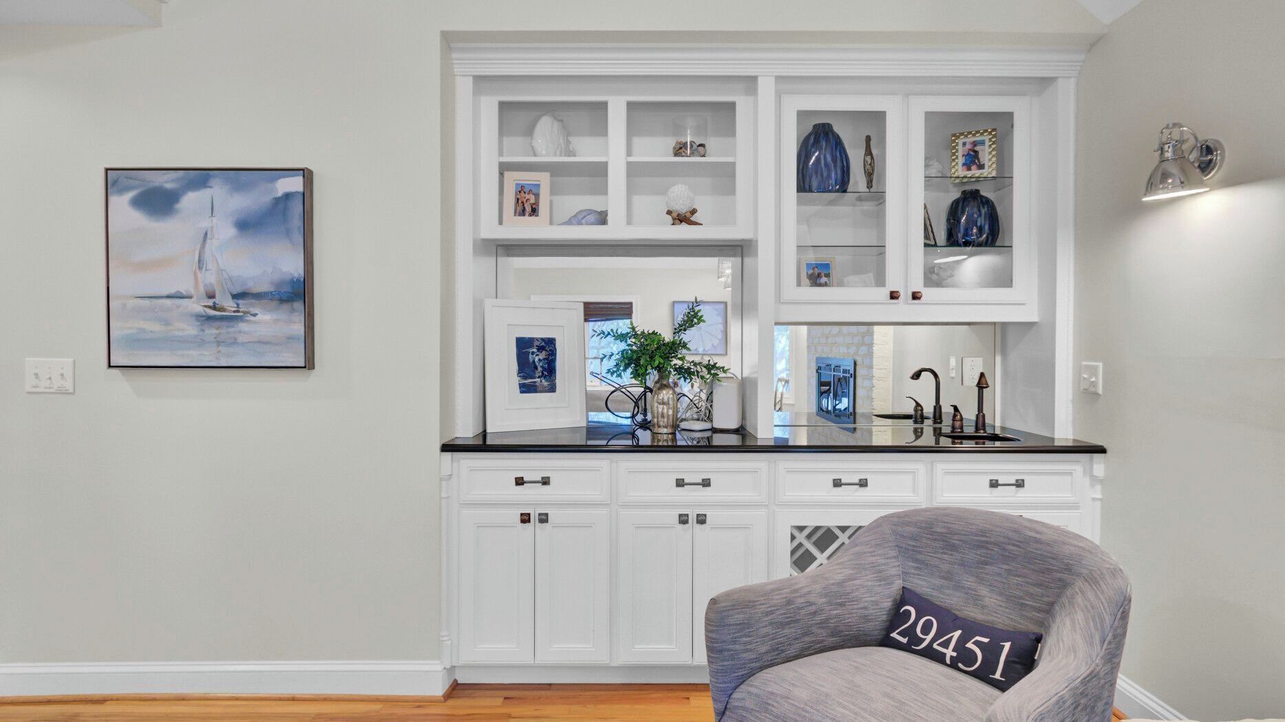 A kitchen with white cabinetry, a black countertop, and a chair with a pillow labeled '29451'.