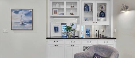 A kitchen with white cabinetry, a black countertop, and a chair with a pillow labeled '29451'.