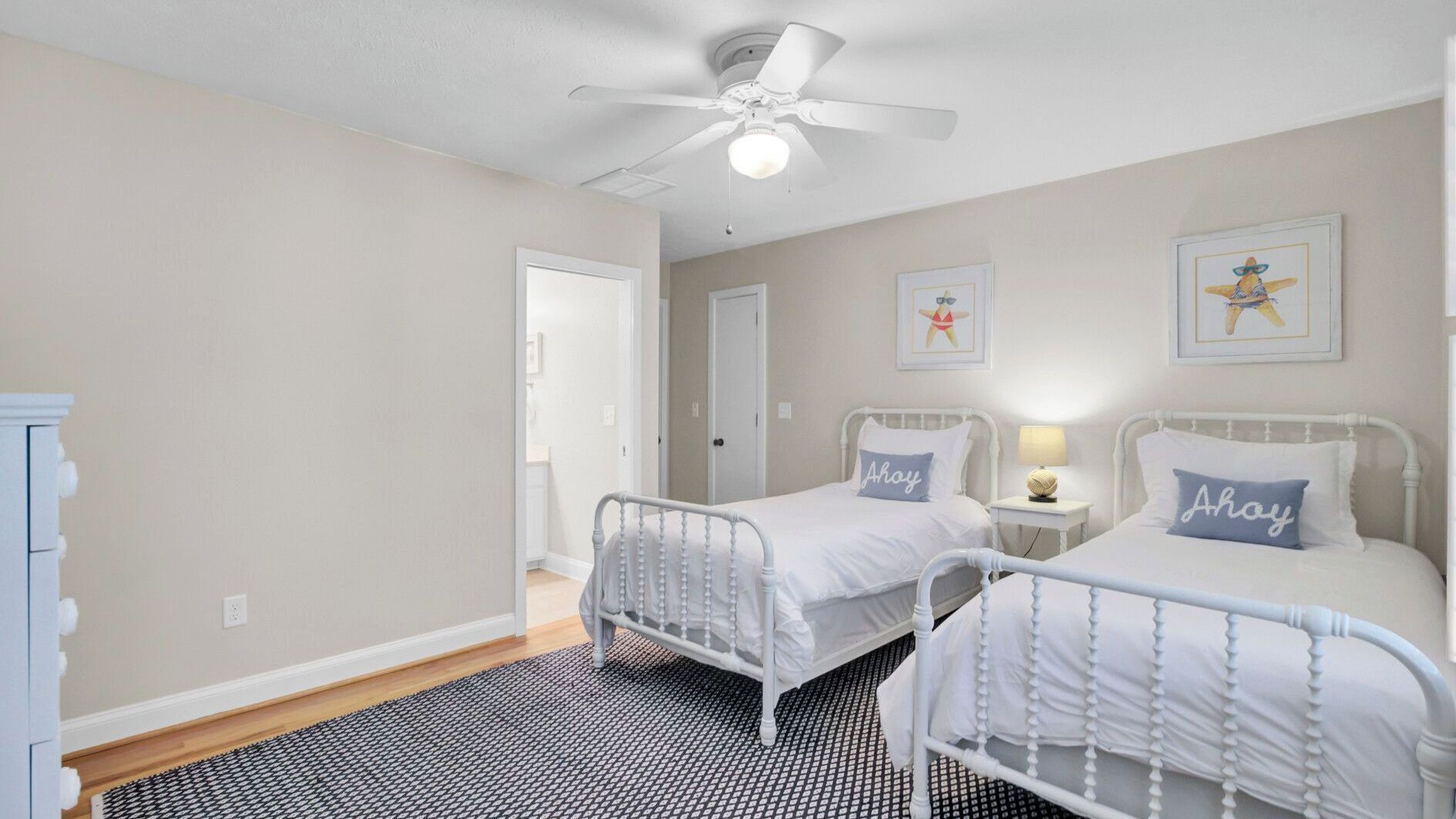 A bedroom with two beds, a ceiling fan, and artwork on the walls.
