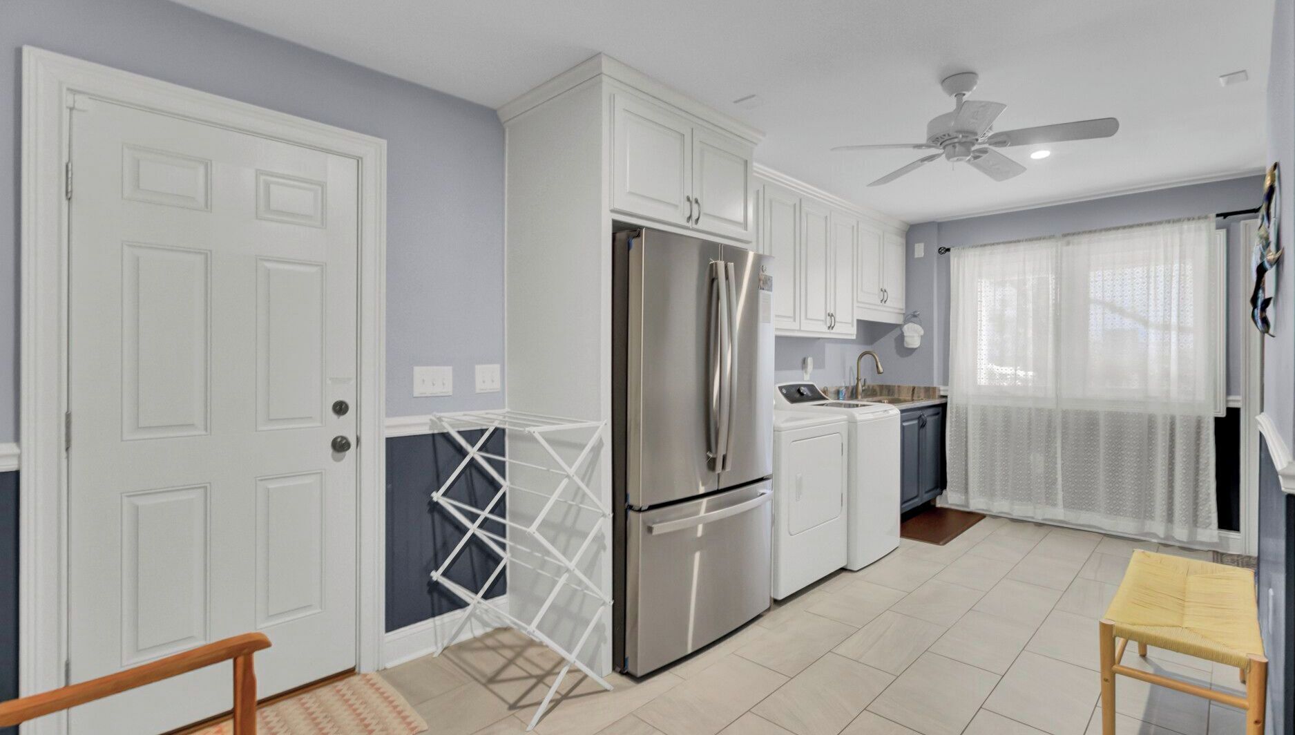A compact kitchen with white cabinets, a stainless steel refrigerator, a washing machine, and a ceiling fan.