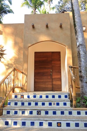 A staircase leading to a wooden door with a beige wall and a palm tree nearby. - San Pancho Jungle Retreat : Private Pool : Casa Coquitos (San Francisco)