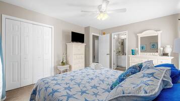 Un dormitorio con cama, ventilador de techo, cómoda, televisor y espejo.