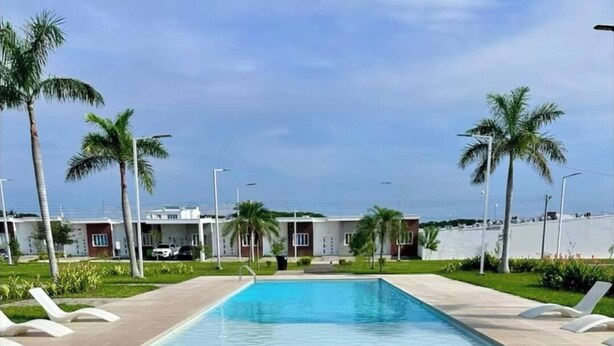 Une piscine rectangulaire à l’eau d’un bleu limpide, entourée d’une terrasse carrelée et de chaises longues blanches. On aperçoit des palmiers à l’arrière-plan.