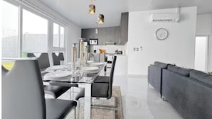 Un espace de salle à manger moderne avec une table en verre, des chaises noires et des luminaires suspendus.
